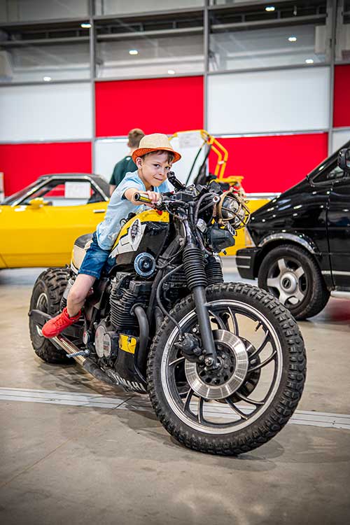 Mały chłopiec pozujący na motocyklu podczas targów motoryzacyjnych.