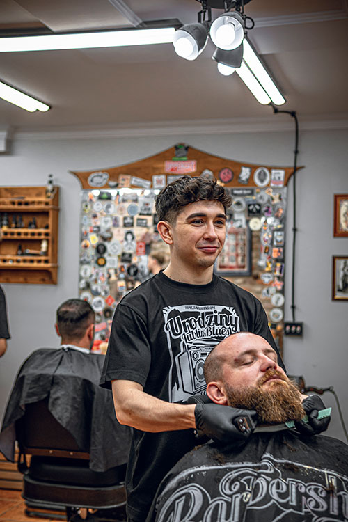 Młody barber masujący głowę zrelaksowanego klienta, z widocznym zaangażowaniem i troską o dobre samopoczucie.