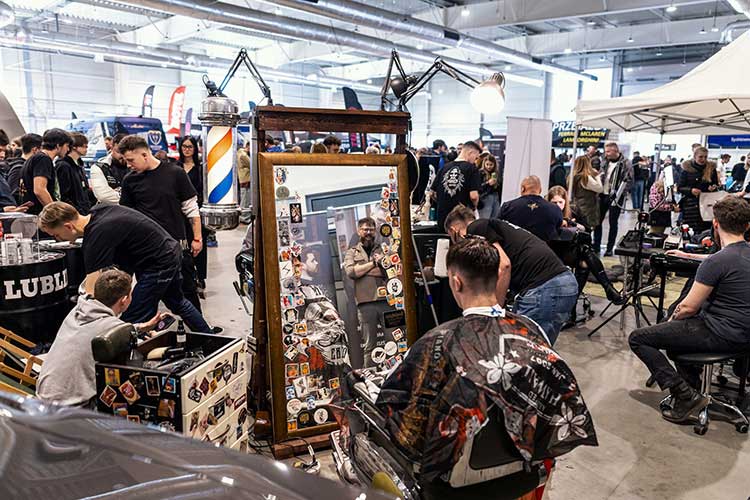 Kadr z tłumem, pełne obłożenie przy stoisku – lustro, sprzęt i robota w toku.