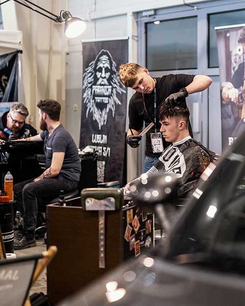 Dwie stacje, pełna koncentracja – barber tnie, w tle tatuaże i rozmowy.