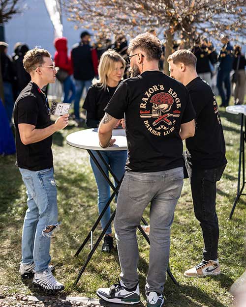 Zespół Razor’s Edge rozmawia przy stoliku na zewnątrz – luz, słońce i ubrano na czarno ekipa z barbershopu.
