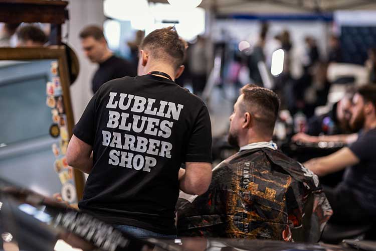 Barber z napisem Lublin Blues Barber Shop na plecach w trakcie cięcia.