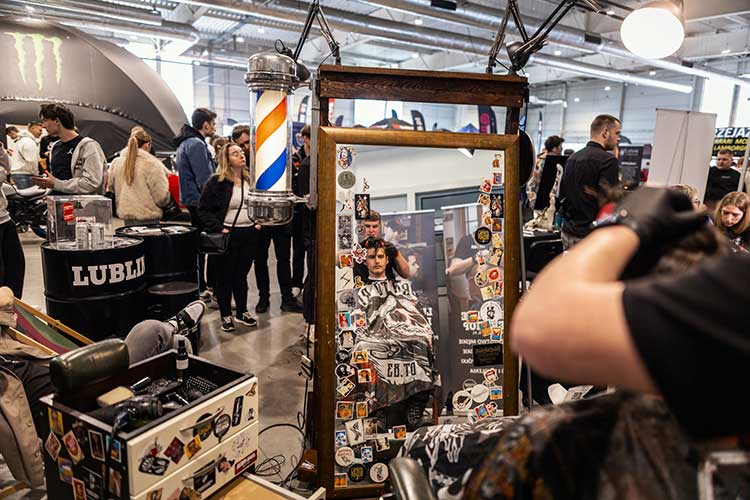 Lustro z naklejkami, cięcie w toku – obok lampa barberpole i ludzie z ciekawością zaglądają.