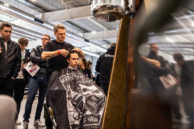 Cięcie pod presją tłumu – barber pracuje przy młodym kliencie, obok zaciekawieni widzowie.