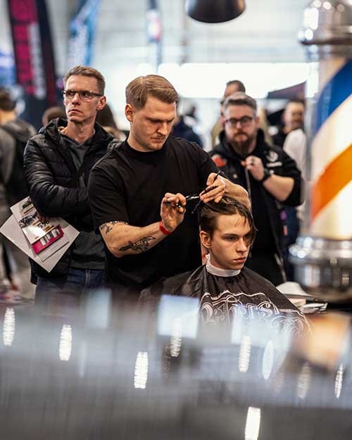 Kultowa lampa barberpole, cięcie na pierwszym planie, a w tle uważni obserwatorzy.