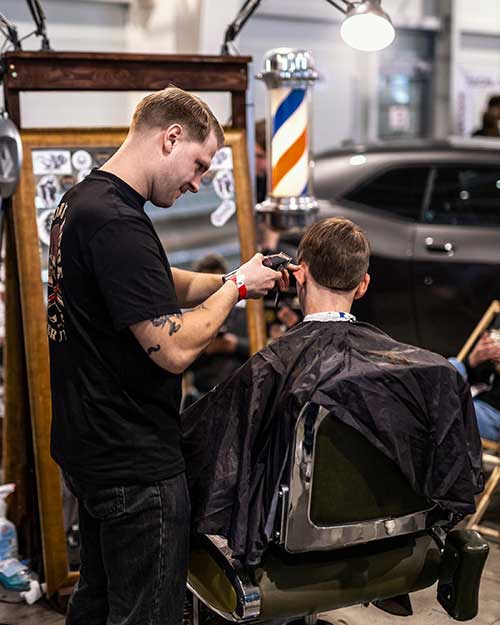 Barber tnie z uśmiechem – klasyczne cięcie przy lustrze. W tle barberpole.