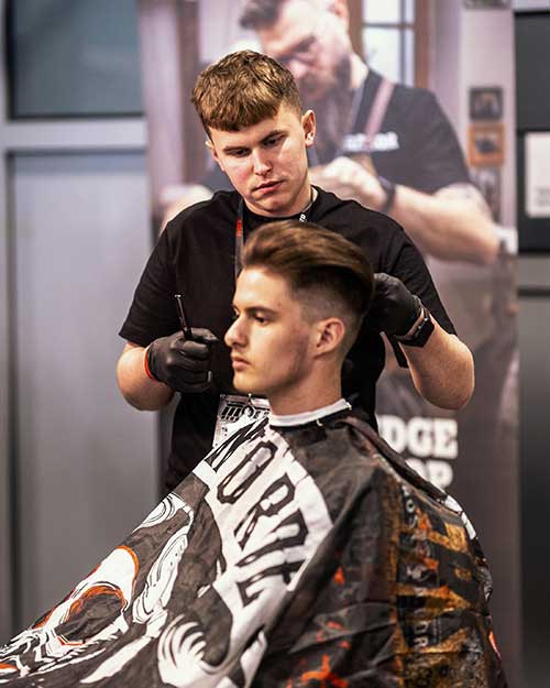 Barber kończy stylizację – idealny fryz i skupienie w oczach, w tle baner Razor’s Edge.